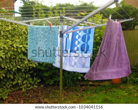 Washed towels blowing and drying in fresh air on garden rotary dryer on windy day 