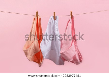 washed women's panties made of cotton with clothespins hanging on a rope on a pink background