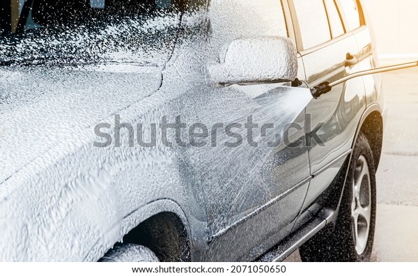 Washing car with active foam shampoo\
outdoors in summer in car wash station. Car exterior covered with\
layer of soft foam and foam spraying from\
hose.