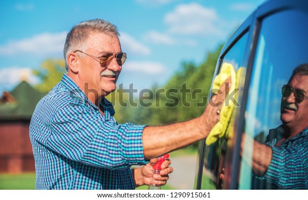 Washing a car. Senior man polishing his car with\
microfiber cloth