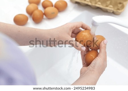 Washing chicken brown organic eggs under running water in sink, health care and salmonella protection concept