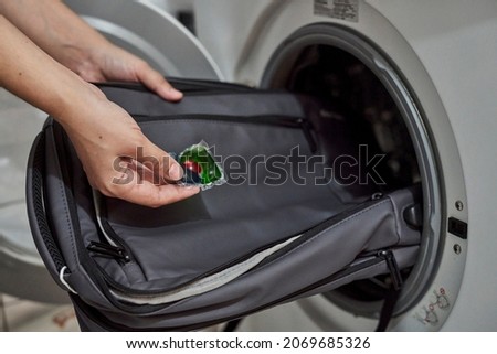 Washing and cleaning backpack in washing machine. Loading dirty school backpack into washing machine. Clean backpack. Washing school bag. Person places backpack in wash machine