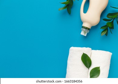 Washing detergent in bioplastic bottle with green leaves on blue background, top view, copy space. Eco recycling cleaning product, eco lifestyle.