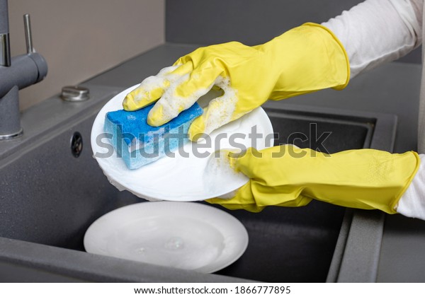 washing dishes\
White plate with detergent and a blue sponge for dishes against the\
background of the\
sink.	