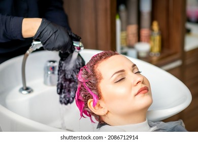 Washing dyed female hair. Professional hairdresser washes pink color paint off of a customer. Young caucasian woman having her hair washed in a beauty salon - Powered by Shutterstock