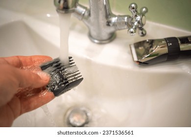 Washing the electric shaver nozzle under the tap.Disinfection of the barber's tool under a stream of water in the faucet. Cleaning the razor for cutting hair. - Powered by Shutterstock