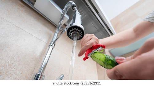 Washing a fresh cucumber under running water with a vegetable peeler for healthy cooking preparation. - Powered by Shutterstock