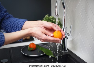 Washing fruit under water.
Woman's hands wash an orange under running tap water.