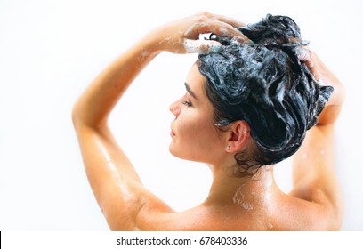 Мытье волос. Красивая голая молодая женщина улыбается и использует шампунь во время принятия душа в ванной комнате. красота сексуальная модель девушка мывает длинные черные волосы. Изолированные на белом фоне