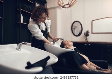 Washing hair, women or stylist with client in salon or basin for scalp care or cleaning treatment. Rinse, healthy or grooming service for customer or shampoo cosmetics for beauty, wellness or spa - Powered by Shutterstock