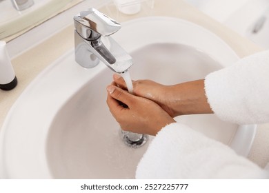 Washing hands of biracial woman in bathrobe in sunny bathroom. Lifestyle, self care, hygiene and domestic life, unaltered. - Powered by Shutterstock