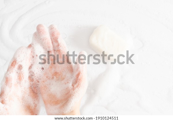 Washing of hands\
with soap, foam. Cleaning hands. Closeup on woman hands with foam\
soap bar on white\
background.