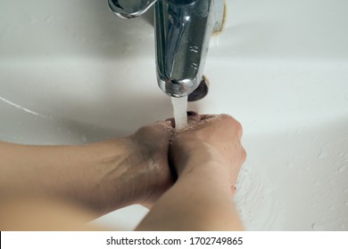 Washing hands under flowing tap water.