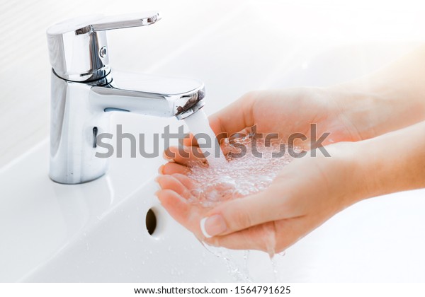 Washing hands under the water tap or\
faucet without soap. Hygiene concept detail. Beautiful hand and\
water stream in bathroom. New modern basin\
cleaning.