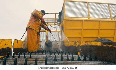 Washing large dirty agricultural machinery. Sugar beet harvesting trailer washer. Worker cleaning industrial equipment with high-pressure hose. A worker in protective gear operates a high-pressure - Powered by Shutterstock