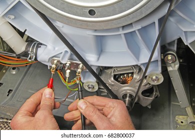 Washing machine appliance repair – Domestic electrical appliance technician holding multimeter probes onto a heating element to test for continuity