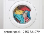 Washing machine with clothes and toy bunny as background, closeup