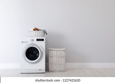 Washing machine with laundry and basket near wall. Space for text