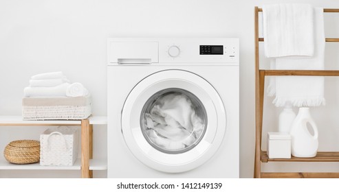 Washing machine with laundry and shelves on white wall background