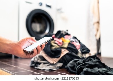 Washing Machine, Phone And Laundry. Smart Home Technology And Smartphone. Person Using Cellphone Or Texting While Doing House Chores. Pile Of Dirty Clothes. Digital Online Equipment In Housework.