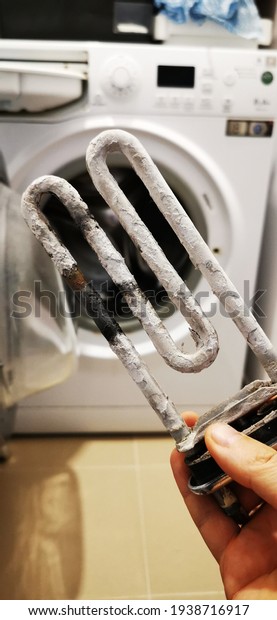 Washing machine repair. A man holds\
in his hand an old, faulty heating element of a wash.\
