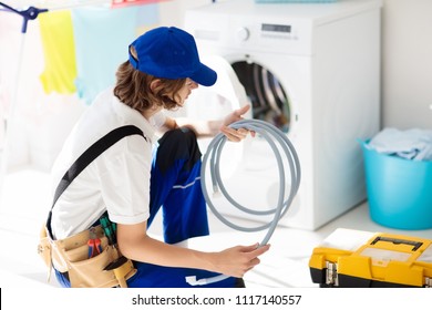 Washing Machine Repair Service. Young Male Technician In Blue Uniform Examining And Repairing Broken Washer Or Tumble Dryer. Maintenance Of Home And Household Appliance. Plumber Apprentice At Work.