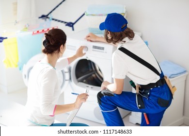 Washing Machine Repair Service. Young Technician Examining And Repairing Tumble Dryer. Woman Looking At Broken Household Appliance. Plumber With Customer. Man Fixing Washer.