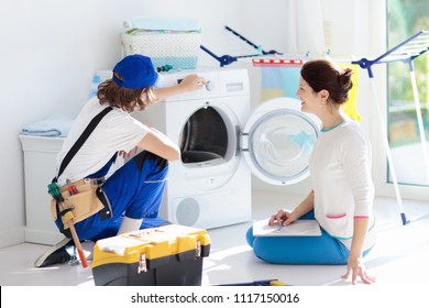 Washing Machine Repair Service. Young Technician Examining And Repairing Tumble Dryer. Woman Looking At Broken Household Appliance. Plumber With Customer. Man Fixing Washer.