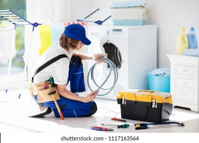 Washing Machine Repair Service. Young Male Technician In Blue Uniform Examining And Repairing Broken Washer Or Tumble Dryer. Maintenance Of Home And Household Appliance. Plumber Apprentice At Work.