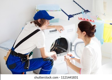 Washing machine repair service. Young technician examining and repairing tumble dryer. Woman looking at broken household appliance. Plumber with customer. Man fixing washer. - Powered by Shutterstock