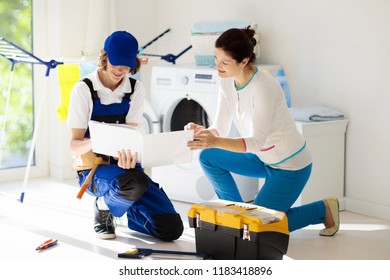 Washing Machine Repair Service. Young Technician Examining And Repairing Tumble Dryer. Woman Looking At Broken Household Appliance. Plumber With Customer. Man Fixing Washer.