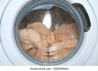Washing machine wrings out the laundry beige bed linen, closeup window view. Modern technologies in everyday life, housework and household. End of washing drum in frame is rotating very quickly.
