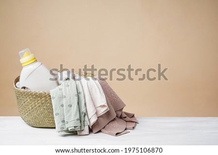 Washing mockup beige background. A basket of colored laundry, a bottle of liquid detergent or fabric softener on a white table with copy space.