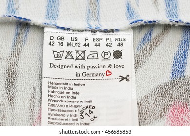 Washing Multilingual Label Text Designed With Passion&love In Germany, Made In India, Size In Several Languages, Icon Iron, Scissors, Heart, Dry Cleaning, Drying On Shirt Wrong Side Fabric Background