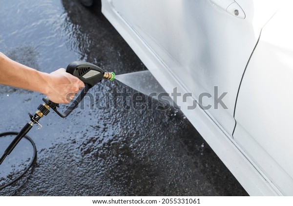 Washing the side\
skirt of a white car with a high pressure water spray gun. At a\
carwash or auto detailing\
shop.