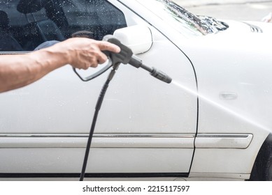 Washing The Side Of A White Car With A High Pressure Water Spray Gun. At A Carwash Or Auto Detailing Shop.