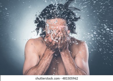 Washing up. Young shirtless man washing face with water splashing around him 