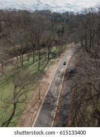 WASHINGTON, DC - MARCH 2017: Lone Car On Lonesome Highway In Wooded Rock Creek, Stark Trees, Distant Skyline, Road Less Traveled.  Rock Creek Is Welcome Green Swath In Urban Setting.