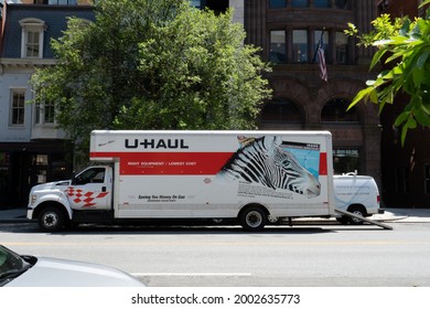 Washington, DC, US - June 23, 2021: A long UHaul truck with metal ramp down is double parked in street and crew of people are unloading boxes furniture at moving destination of new district resident