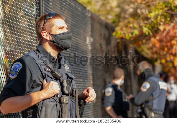 Washington DC, USA 11-06-2020: Police officer\
wearing face mask due to COVID 19 pandemic and body camera is on\
duty in Black Lives Matter Plaza near White House attending\
demonstration on a sunny\
day.