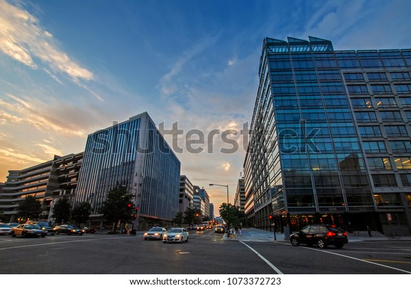 Washington, DC,\
USA - August 04, 2012: beautiful sunset on Pennsylvania Avenue NW\
and 19th NW Street crossroad with traffic and Global Environment\
Facility and Passport Services buildings\
