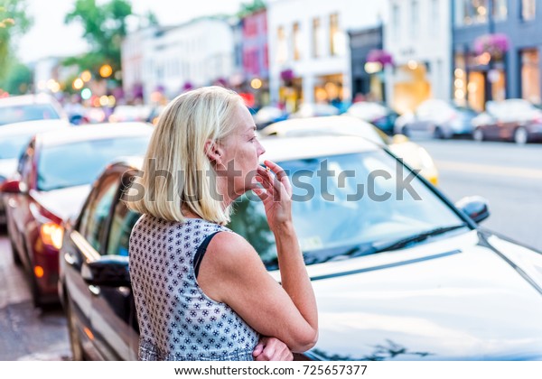Washington DC, USA -\
August 4, 2017: Back of middle aged woman in 50s smoking cigarette\
looking at downtown Georgetown neighborhood street and brick\
buildings, stores in\
evening