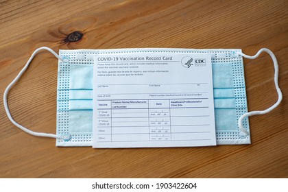 Washington, DC, USA - December, 23, 2020: Covid-19 Vaccination Record Card By CDC Covered Blue Medical Mask. 