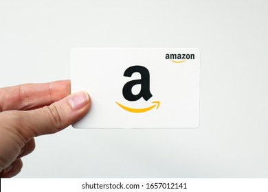 Washington, D.C. / USA - Feb. 26, 2020: A woman's hand holds a white Amazon.com gift card against a plain background. The card can be used to make purchases on the Amazon website.