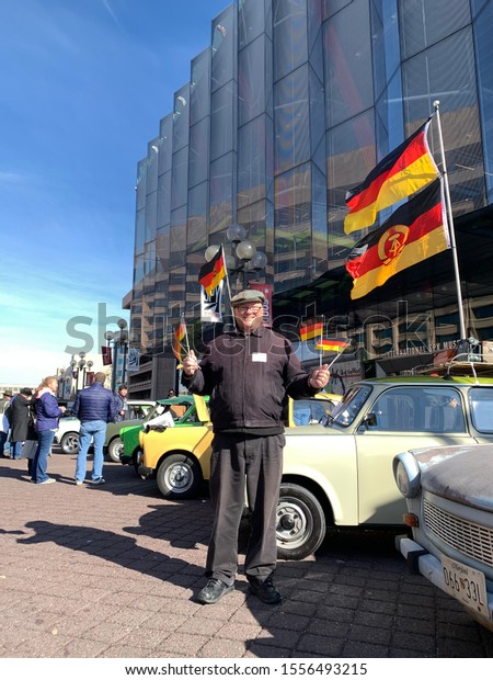 Washington,\
DC / USA - November 9, 2019: Man waving German flags in front of a\
Trabant car at the International Spy Museum as part of the 30th\
anniversary of the Fall of the Berlin Wall.\
