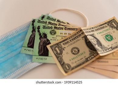 Washington, Usa - 10 March 2021: Close Up Of Stimulus Check And Face Mask And Banknote On Black Background, Concept Of Federal Financial Help Given To Stop Economic Crisis On White Background