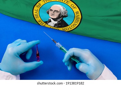 Washington Vaccination. Hands Of Doctor Holding Syringe And Coronavirus (COVID-19) Vial Vaccine On Flag Washington