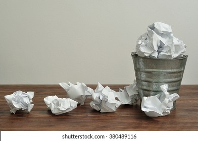 A waste bucket overflowing with crumbled up pieces of paper