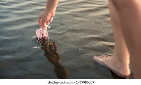 Waste during COVID-19. Volunteer woman cleaning up the beach. The volunteer raises a coronavirus single-use face masks garbage from the water. Environmental awareness concept - Powered by Shutterstock