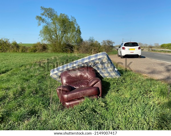 Waste furniture fly tipped on the road side, car in\
background. Landscape\
view